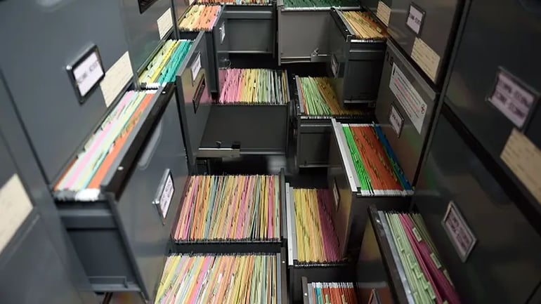 A ROOM OF FILING CABINETS, WITH SEVERAL DRAWERS OPEN THAT ARE FILLED WITH FILES. 