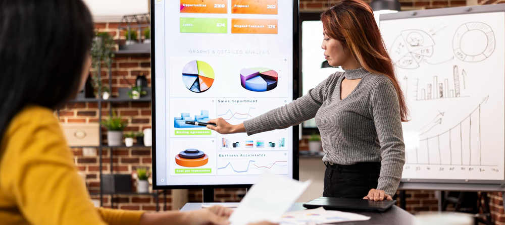 Duas colaboradoras analisando gráficos em uma grande tela