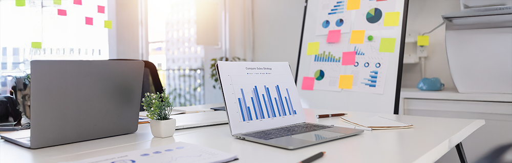 Imagem de notebooks em uma mesa, com gráficos apresentados, post-its marcando gráficos