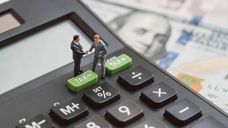 TWO SMALL CHARACTER-LIKE BUSINESSMEN SHAKING HANDS, STANDING ON AN OVERSIZED CALCULATOR. 