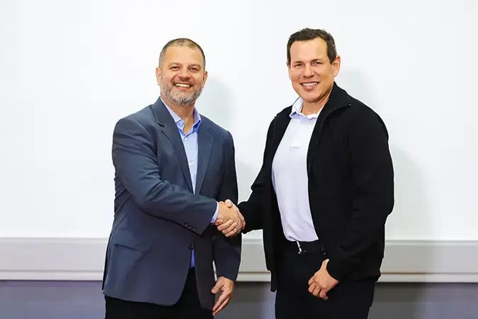 Foto da inauguração do novo escritório de SAP B1 em Curitiba. Ao lado esquerdo, vestindo um terno cinza, está Felipe Jacob, vice presidente de operações. Ao lado direito, de terno preto, está Luis Diaz, presidente da divisão de tecnologia. Os dois se cumprimentam com um aperto de mão, simbolizando união. 