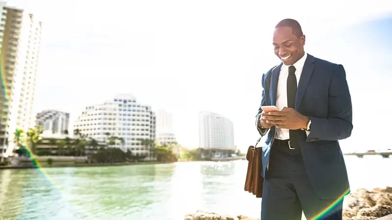 Hombre de negocios en un traje azul sonriendo mientras envía mensajes de texto en Miami, Florida