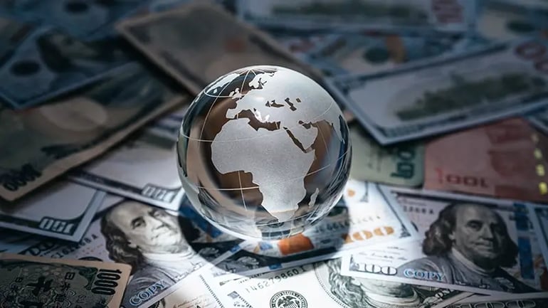 A GLASS GLOBE SITTING ON A PILE OF CURRENCY FROM DIFFERENT COUNTRIES. 