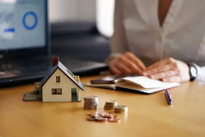 Na foto, há uma mesa, com moedas e uma miniatura de casa simbolizando os bens pessoais. 