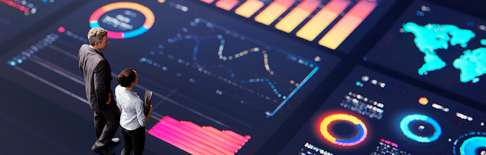 Dois consultores analisando gráficos em uma tela gigante 
